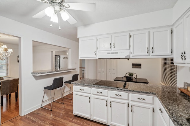 kitchen with black electric cooktop, wood-type flooring, white cabinets, and dark stone counters