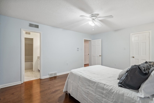 bedroom featuring ceiling fan, ensuite bathroom, dark hardwood / wood-style flooring, and a textured ceiling