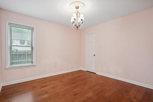 empty room with dark hardwood / wood-style flooring and a notable chandelier