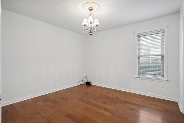 empty room featuring dark hardwood / wood-style flooring and an inviting chandelier