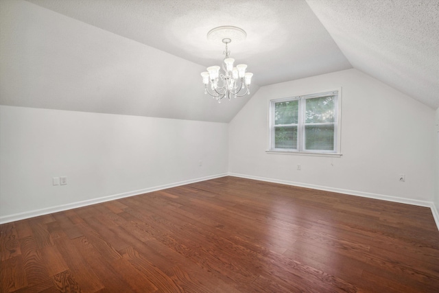 additional living space with a textured ceiling, dark wood-type flooring, vaulted ceiling, and an inviting chandelier