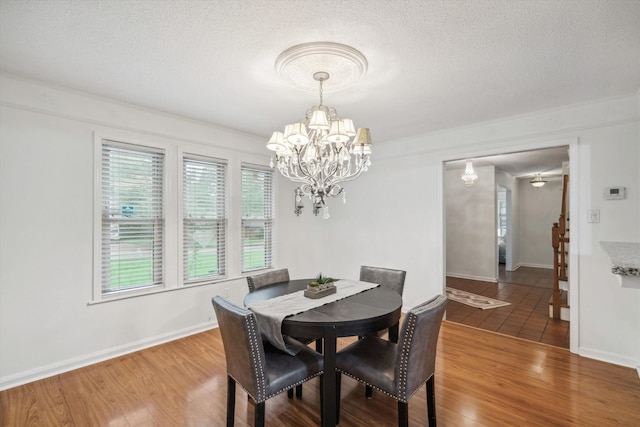 dining space featuring a textured ceiling, hardwood / wood-style floors, ornamental molding, and an inviting chandelier