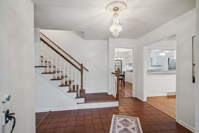 foyer entrance featuring dark tile patterned flooring, a textured ceiling, and an inviting chandelier