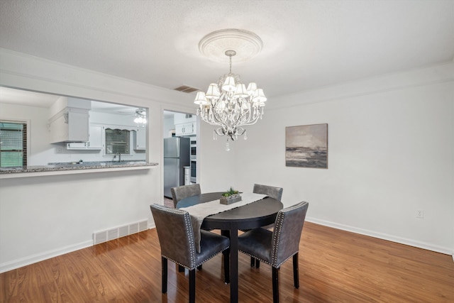 dining area with a textured ceiling, ceiling fan with notable chandelier, ornamental molding, and light hardwood / wood-style floors