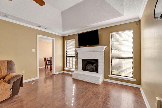 living room with a raised ceiling, a fireplace, wood-type flooring, vaulted ceiling, and ornamental molding