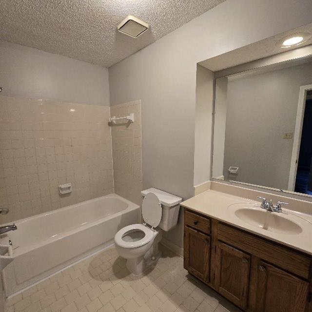 full bathroom featuring a textured ceiling, toilet, vanity, and tiled shower / bath