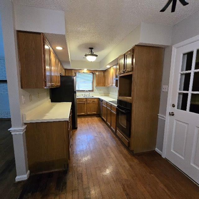 kitchen with sink, a textured ceiling, black appliances, and dark hardwood / wood-style flooring