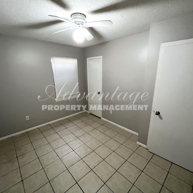 empty room with ceiling fan, light tile patterned floors, and a textured ceiling