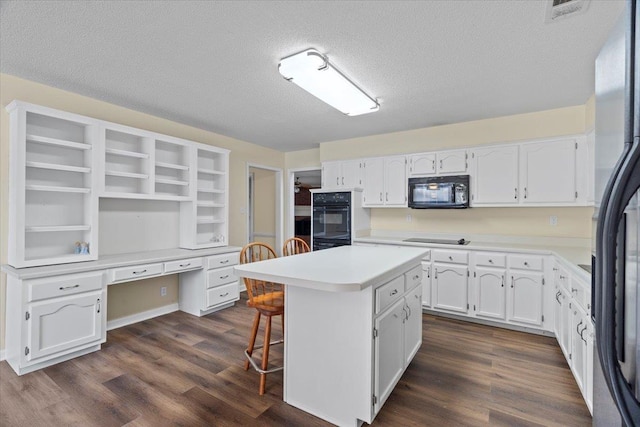 kitchen with a kitchen island, black appliances, built in desk, a textured ceiling, and white cabinets