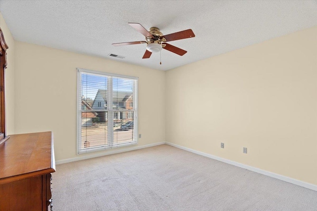 empty room with ceiling fan, light colored carpet, and a textured ceiling