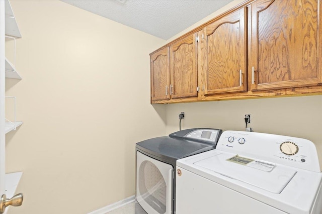 clothes washing area with washing machine and dryer, a textured ceiling, and cabinets