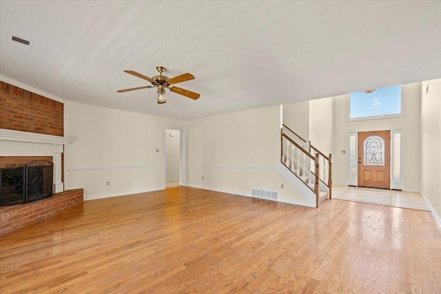 unfurnished living room featuring ceiling fan, a brick fireplace, a textured ceiling, and light hardwood / wood-style flooring