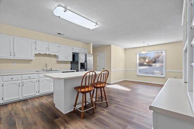 kitchen featuring white cabinets, a center island, stainless steel refrigerator with ice dispenser, decorative light fixtures, and sink