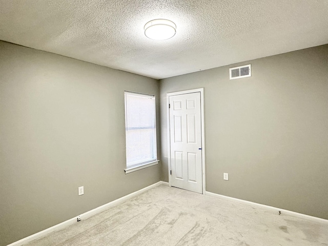 unfurnished room with light colored carpet and a textured ceiling