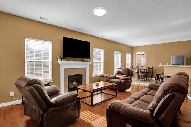 living room with a tile fireplace, light hardwood / wood-style flooring, a textured ceiling, and a notable chandelier