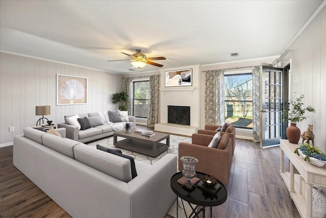 living room featuring a textured ceiling, dark hardwood / wood-style flooring, ornamental molding, and a brick fireplace