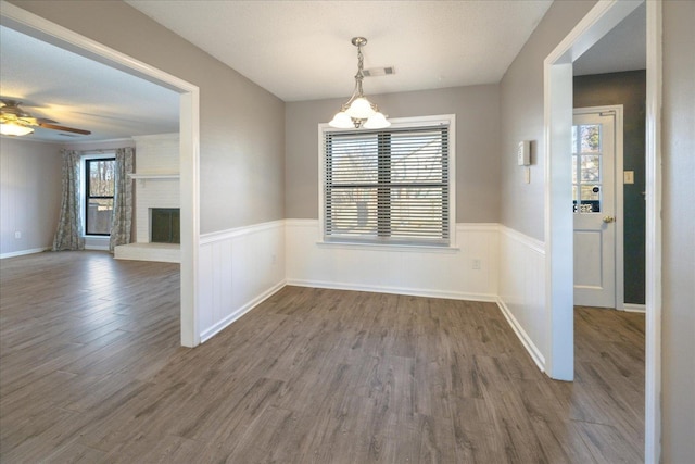 unfurnished dining area featuring ceiling fan, a brick fireplace, and hardwood / wood-style floors