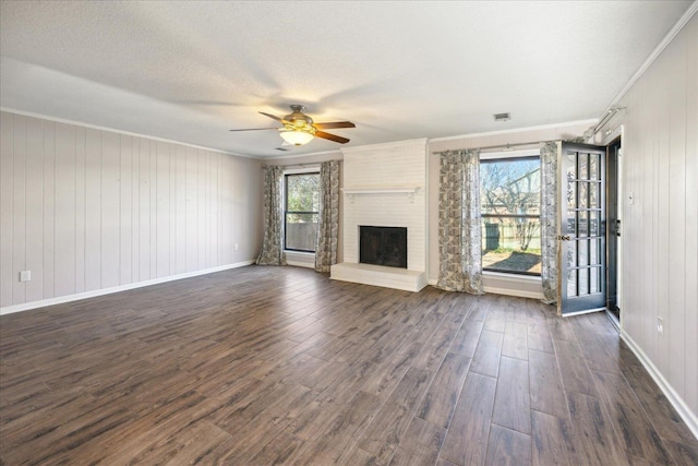 unfurnished living room with a fireplace, a healthy amount of sunlight, dark hardwood / wood-style flooring, and crown molding