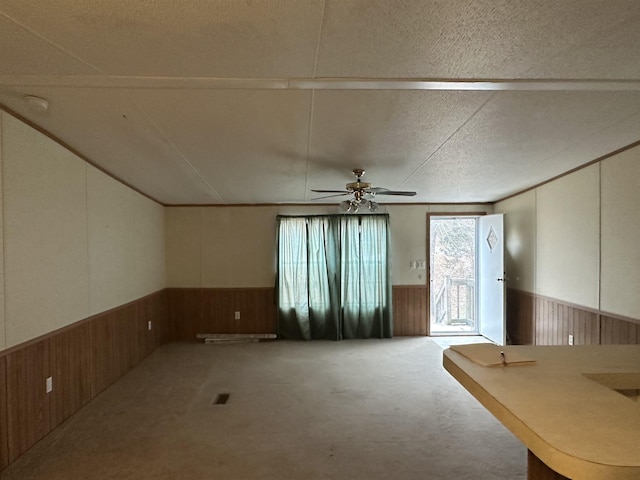 carpeted spare room with a textured ceiling, ceiling fan, and wood walls