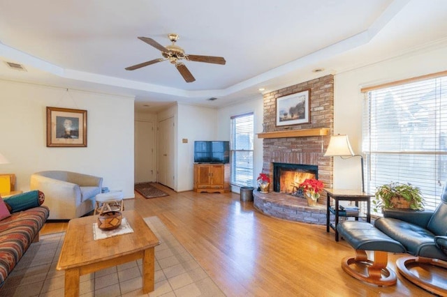 living room with ceiling fan, wood-type flooring, a tray ceiling, and a fireplace