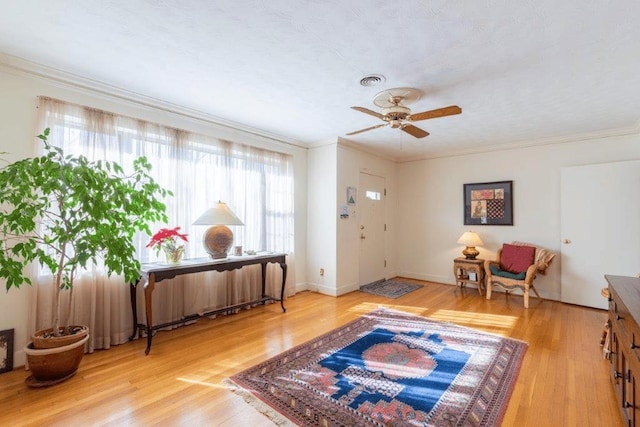 living area with light wood-type flooring, ceiling fan, and crown molding