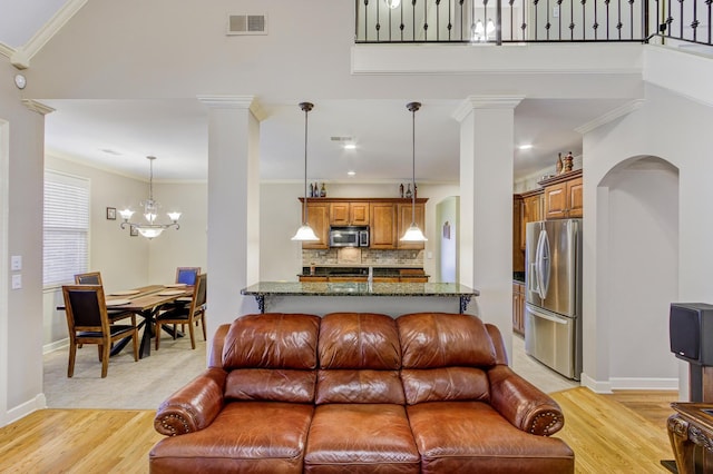 living room with light wood-type flooring, ornamental molding, a notable chandelier, and ornate columns