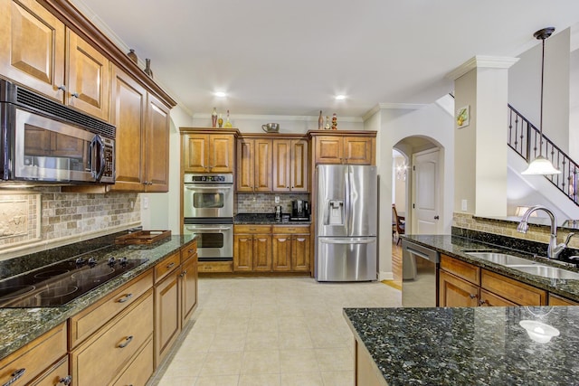 kitchen featuring appliances with stainless steel finishes, sink, dark stone countertops, ornamental molding, and pendant lighting