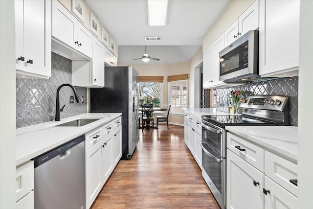 kitchen with white cabinets, appliances with stainless steel finishes, ceiling fan, sink, and light stone counters