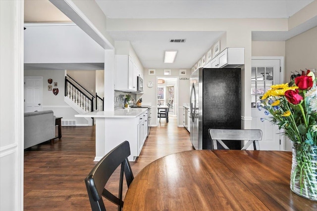 kitchen featuring stainless steel appliances, white cabinetry, kitchen peninsula, and dark hardwood / wood-style flooring