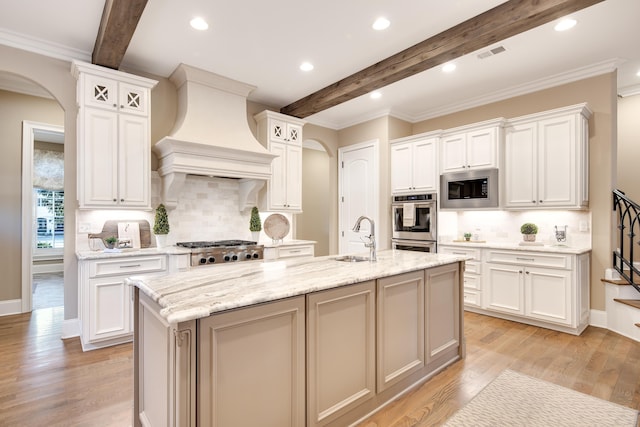 kitchen with appliances with stainless steel finishes, wall chimney exhaust hood, sink, white cabinetry, and a center island with sink