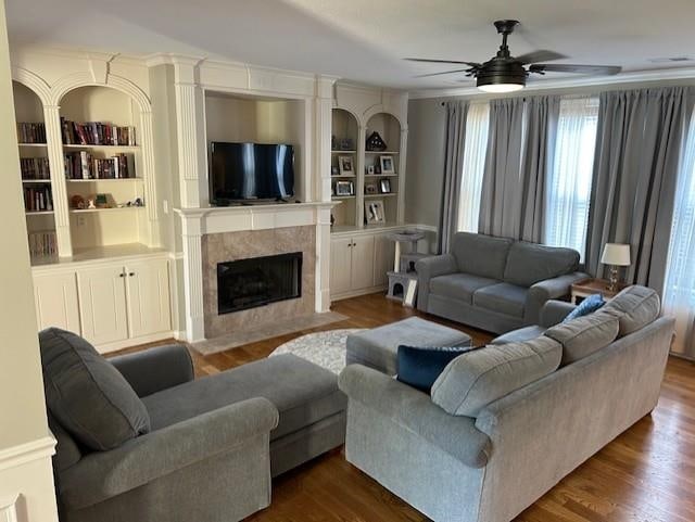 living room featuring built in features, hardwood / wood-style flooring, ceiling fan, and a fireplace