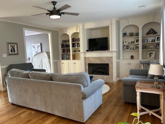 living room featuring built in features, wood-type flooring, ornamental molding, and a tiled fireplace