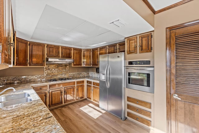 kitchen with light hardwood / wood-style floors, sink, backsplash, stainless steel appliances, and light stone counters