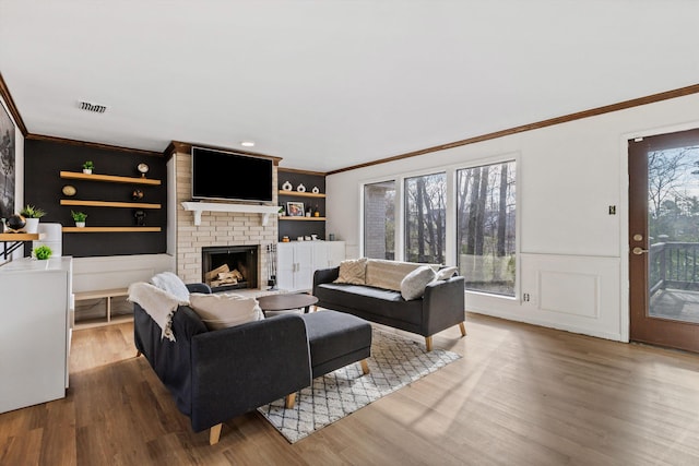 living room with a fireplace, built in features, wood-type flooring, and ornamental molding