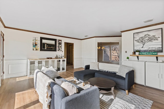 living room featuring light wood-type flooring, an inviting chandelier, and ornamental molding