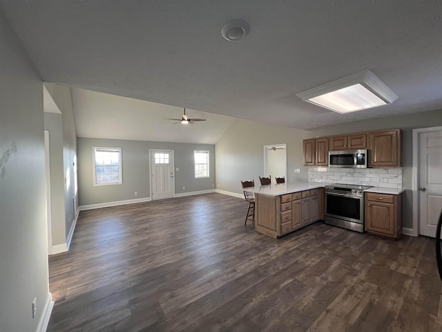 kitchen with appliances with stainless steel finishes, lofted ceiling, decorative backsplash, kitchen peninsula, and ceiling fan