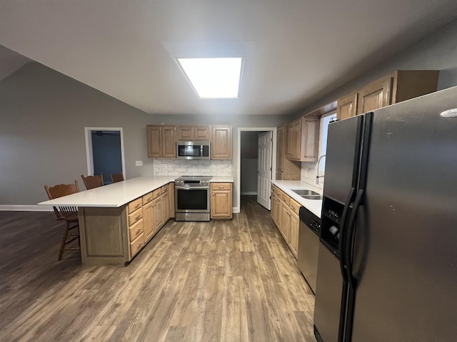 kitchen featuring a kitchen bar, stainless steel appliances, tasteful backsplash, kitchen peninsula, and hardwood / wood-style flooring