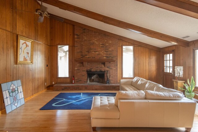 living room with a brick fireplace, vaulted ceiling with beams, light hardwood / wood-style floors, and wooden walls