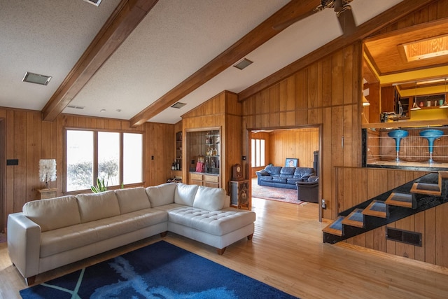 living room featuring light wood-type flooring, wood walls, a textured ceiling, and lofted ceiling with beams