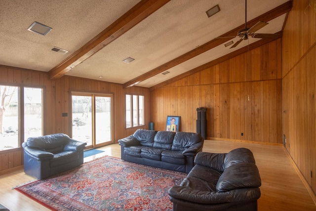 living room with light hardwood / wood-style floors, a textured ceiling, ceiling fan, wood walls, and lofted ceiling with beams