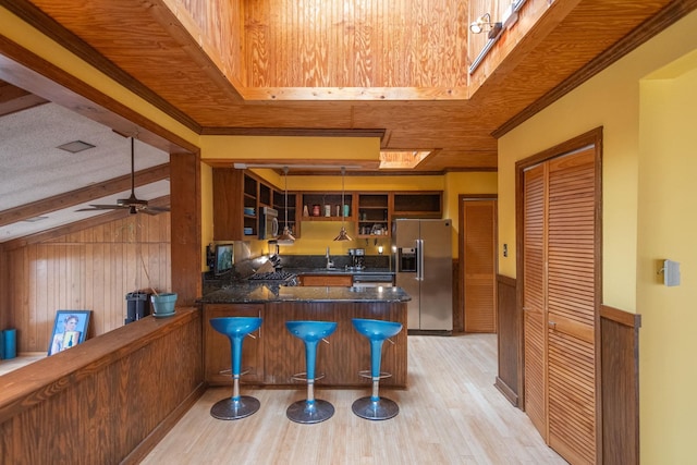 kitchen featuring wood walls, hanging light fixtures, appliances with stainless steel finishes, and kitchen peninsula