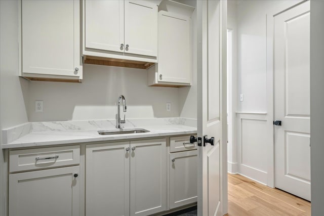 kitchen featuring sink, light wood-type flooring, white cabinets, and light stone countertops