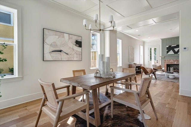 dining space featuring light hardwood / wood-style floors, ornamental molding, a chandelier, a brick fireplace, and coffered ceiling