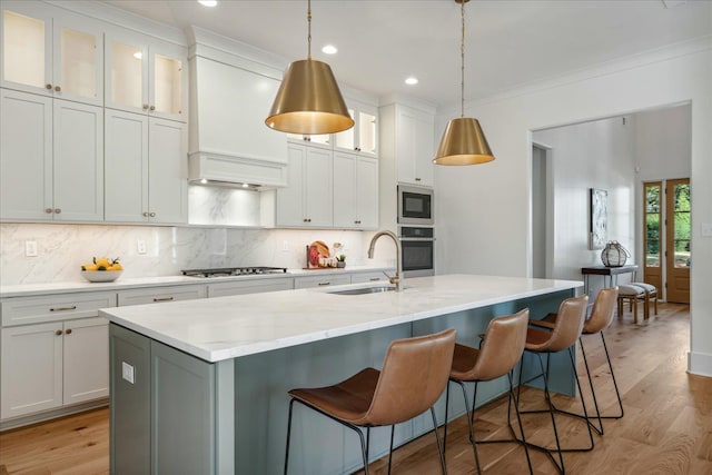 kitchen with pendant lighting, appliances with stainless steel finishes, white cabinetry, sink, and a kitchen island with sink