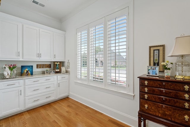 interior space featuring light stone countertops, white cabinetry, ornamental molding, and light wood-type flooring