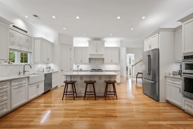 kitchen with light hardwood / wood-style flooring, appliances with stainless steel finishes, white cabinets, a kitchen island, and a breakfast bar area