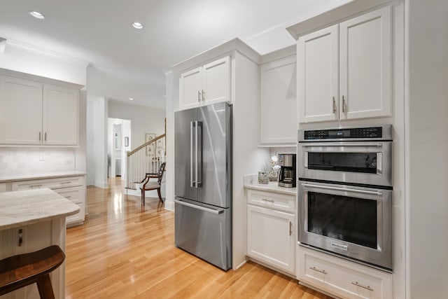 kitchen with backsplash, white cabinetry, light wood-type flooring, and appliances with stainless steel finishes