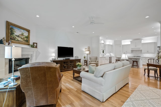 living room featuring sink, ceiling fan, light hardwood / wood-style flooring, and a fireplace