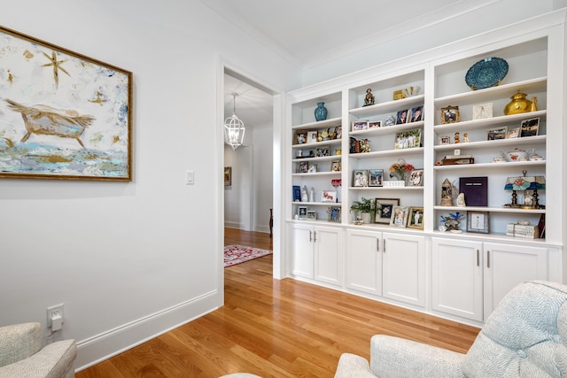 living area with built in features, crown molding, a notable chandelier, and light wood-type flooring