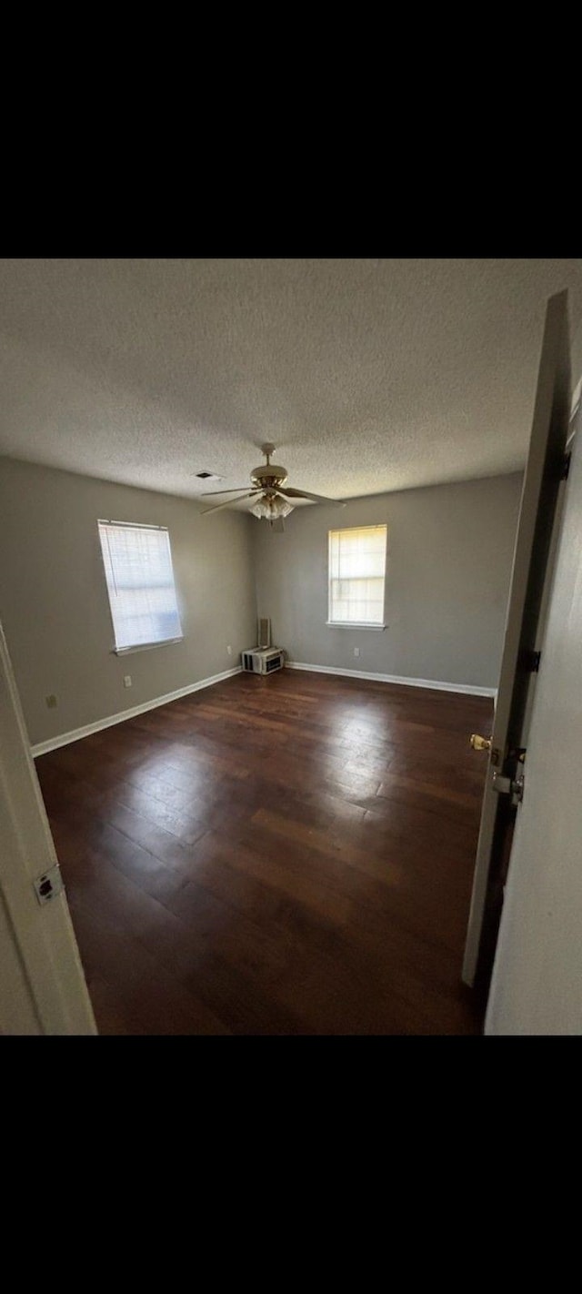 unfurnished room with ceiling fan, dark wood-type flooring, a textured ceiling, and plenty of natural light